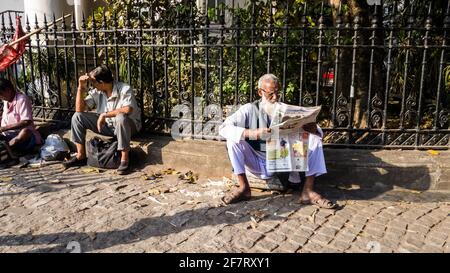 Kolkata, Bengale-Occidental, Inde - janvier 2018 : un Indien âgé assis sur le trottoir et lisant un journal dans la ville de Kolkata. Banque D'Images