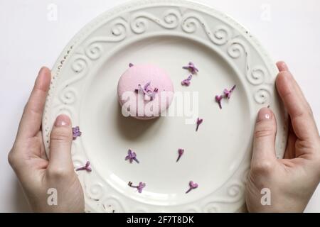 Vue rognée d'une assiette de femme avec un délicieux macaron français rose ou un macaron avec des fleurs de lilas sur fond blanc. Banque D'Images