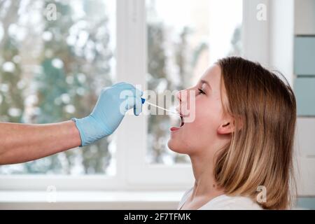 La main du médecin avec un coton-tige prend une analyse de la bouche d'une fille. Banque D'Images