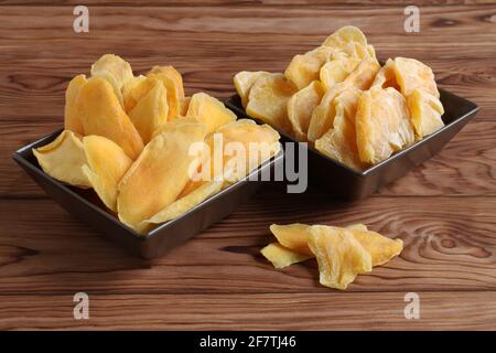 Morceaux séchés de mangue et de jackfruit sur une table en bois, placés sur des bols en céramique marron. Macro. Gros plan Banque D'Images