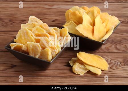 Morceaux séchés de mangue et de jackfruit sur une table en bois, placés sur des bols en céramique marron. Macro. Gros plan Banque D'Images