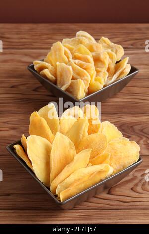 Morceaux séchés de mangue et de jackfruit sur une table en bois, placés sur des bols en céramique marron. Macro. Gros plan Banque D'Images