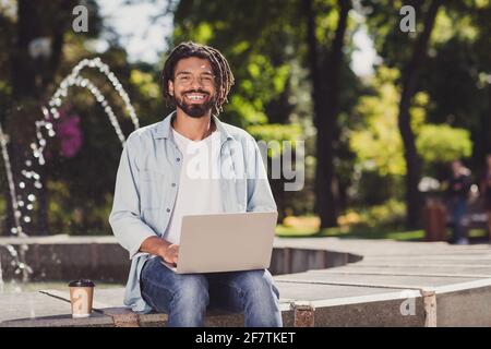 Photo portrait de l'étudiant dans des vêtements décontractés à l'aide d'un ordinateur portable faire projet portant des lunettes buvant du café près de la fontaine Banque D'Images