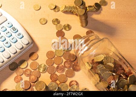 Vue de dessus d'un pot de pièces de monnaie à moitié vide avec des piles de pièces de monnaie et plus de pièces de monnaie sur une table. Bannière de concept d'économie d'argent Banque D'Images