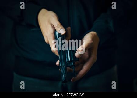 Gros plan du revolver de rechargement manuel. Les mains des hommes vérifient la présence de balles dans le canon. La personne se prépare pour les tirs. Arme à feu pour la défense ou l'attaque. Banque D'Images