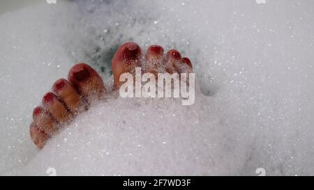 Gros plan sur les ongles peints en rouge des orteils de femme ayant un bain moussant relaxant Banque D'Images