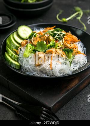 Funchoza avec poulet et légumes sur fond noir, vue du dessus, espace de copie. Nouilles en verre, cuisine asiatique. Banque D'Images