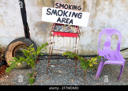 Espace fumeurs improvisé avec un cendrier plein de mégots de cigarettes placés à l'extérieur à côté d'un mur sale, avec une chaise en plastique pour le fumeur, l'Asie Banque D'Images