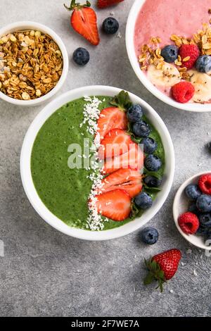 Matcha thé vert petit-déjeuner smoothies saladiers nappés de fraises, bleuets, flocons de noix de coco Overhead, vue de dessus, plat Banque D'Images