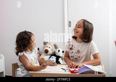 Deux filles caucasiennes, très souriantes, qui sont assises à une table d'enfants, colorant et dessinant des cartes postales et des cadeaux pour leur père le jour du Père. Banque D'Images