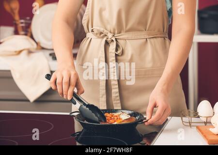 Femme qui cuisine le petit déjeuner anglais traditionnel sur cuisinière électrique dans la cuisine Banque D'Images