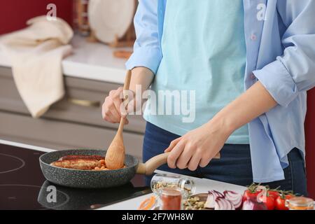 Femme qui cuisine le petit déjeuner anglais traditionnel sur cuisinière électrique dans la cuisine Banque D'Images