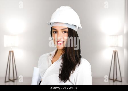 Une femme architecte souriante avec casque de protection dans un salon moderne avec deux lampes. Sujet sur un arrière-plan flou. Photo idéale pour la rénovation Banque D'Images