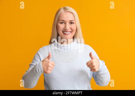 Bonne femme mûre avec beau sourire montrant le pouce sur la couleur arrière-plan Banque D'Images