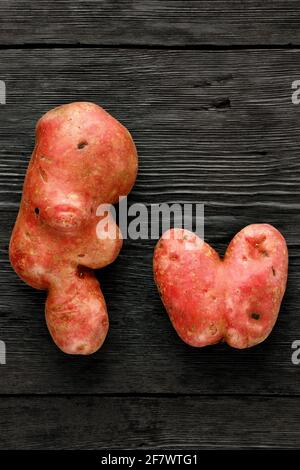 Pommes de terre moches en forme de coeur et en forme torsadée sur fond noir en bois. Concept de légumes ou de déchets alimentaires. Vue de dessus, gros plan. Banque D'Images