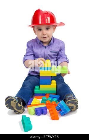 L'enfant s'assoit sur le sol avec des jouets répartis entre ses jambes. Isolé. Banque D'Images