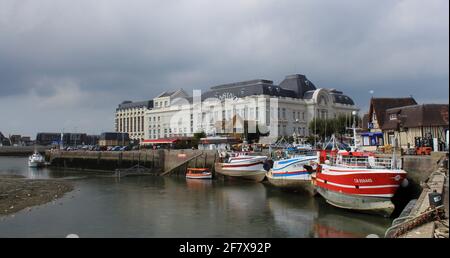 le casino blanc de la côte française de trouville avec des bateaux de pêche colorés dans le port en face en été Banque D'Images