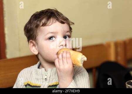 L'enfant mangeant un petit pain au café Banque D'Images