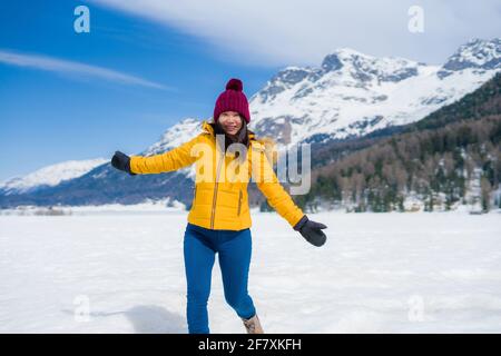 Jeune femme coréenne asiatique heureuse et gaie en veste d'hiver et chapeau jouant sur le lac gelé recouvert de neige Aux montagnes des Alpes suisses appréciant h Banque D'Images