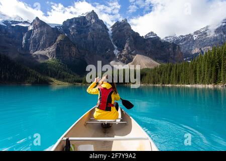 fille en face d'un canoë dans les montagnes portant une veste jaune sur un lac turquoise en été Banque D'Images