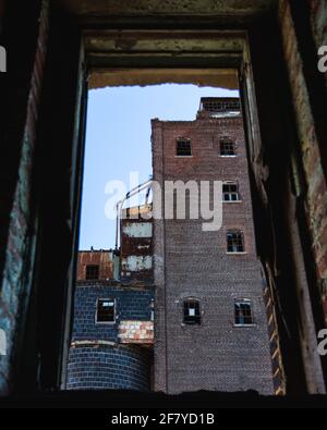 Fenêtre cassée dans un bâtiment abandonné avec vue sur le autre côté avec des briques rouges ni été avec ciel bleu Banque D'Images