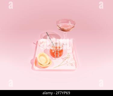 Composition romantique avec un pot de caviar rouge de saumon, tartelettes, vin de rose et fleurs sur un plateau sur fond rose avec des ombres dures Banque D'Images