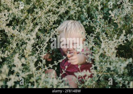 Mignon petit garçon blond jouant dans un Bush dans un stationnement Banque D'Images