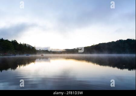 Tôt le matin sur un lac dans la région avec de l'eau calme réflexion de la rive dans la distance Banque D'Images