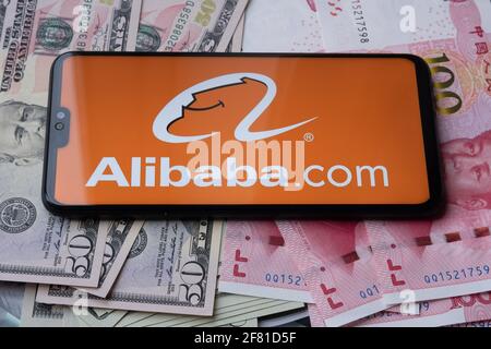 Logo Alibaba vu sur smartphone qui est placé sur l'argent - dollars américains et yuan chinois. Arrière-plan flou. Staffrod, Royaume-Uni, 10 avril 2021. Banque D'Images