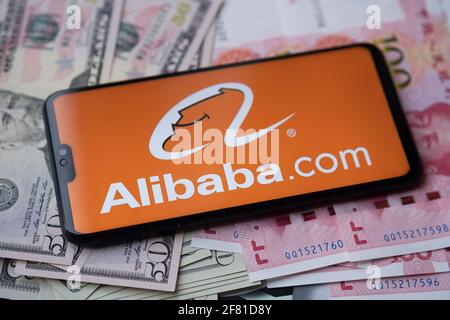 Logo Alibaba vu sur smartphone qui est placé sur l'argent - dollars américains et yuan chinois. Arrière-plan flou. Staffrod, Royaume-Uni, 10 avril 2021. Banque D'Images