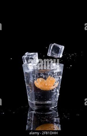 Une photo en studio de glaçons déposés dans un verre d'eau avec une tranche d'orange. Banque D'Images