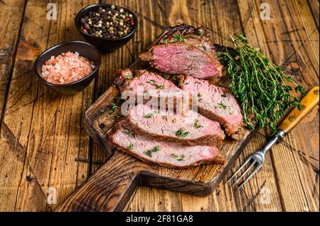 Tranches rares de rôti de boeuf sirloin à trois pointes steak bbq sur une planche à découper en bois. fond en bois. Vue de dessus Banque D'Images