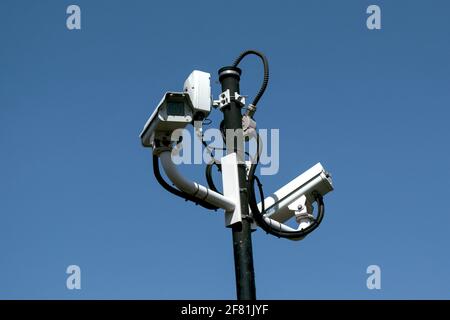 Deux caméras de surveillance blanches et d'autres accessoires de sécurité assortis sur le dessus d'un montant élevé, contre un ciel bleu clair. Ottawa, Ontario, Canada. Banque D'Images