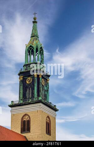 Tour d'horloge ornée de détails dorés, un flèche vert patiné et des fenêtres cintrées sous un ciel bleu parsemé de nuages blancs. Banque D'Images