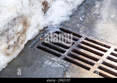 L'eau s'écoule à travers le couvercle du trou d'homme, faisant fondre la neige au printemps. Voir l'eau qui coule dans les eaux usées Banque D'Images