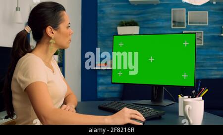 Indépendant assis à la table de bureau et de naviguer sur le réseau pour les affaires de commerce en utilisant l'ordinateur avec maquette écran vert clé chroma. Femme caucasienne travaillant avec un pc isolé dans un appartement de bureau Banque D'Images