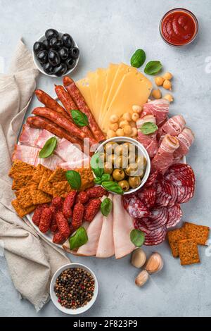 Tranches de saucisse et de fromage sur une planche à découper avec olives et basilic sur fond gris clair. Tableau de charcuterie avec salami, bacon, saucisses à l'ail a Banque D'Images