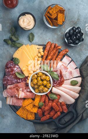 Hors-d'œuvre à la viande, assortiment de saucisses, fromage, olives et basilic sur une planche à découper sur fond gris. Vue verticale, image teintée. Banque D'Images