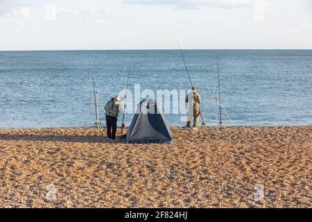 Deux hommes pêchent en mer depuis une plage de galets Banque D'Images