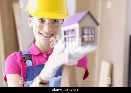 Femme souriante constructeur tenant la maison dans ses mains Banque D'Images