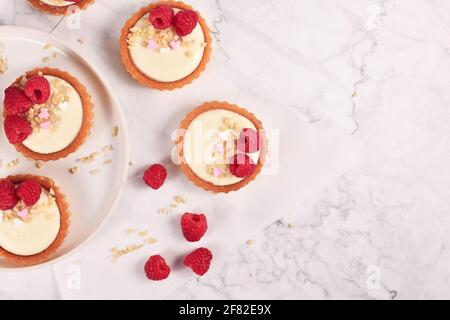 Petites pâtisseries tartelettes à la crème blanche, nappées de fruits à la framboise et de saupoudrés d'amandes Banque D'Images