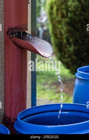 L'eau de pluie s'écoulant du toit s'écoule dans le tonneau du jardin. Gouttes de pluie dans le flou de mouvement. L'aluminium se prépare sous la pluie. Style de vie durable dans le jardin Banque D'Images