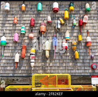 Bouées de homard anciennes et colorées accrochées sur un mur abîmé à Portan Maine avec des pièges jaunes au fond. Banque D'Images