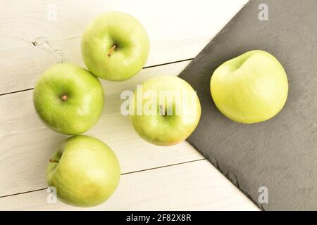 Un groupe de plusieurs pommes biologiques juteuses, mûres, douces, vertes, gros plan, sur le fond d'un plateau de service d'ardoise et d'une table de peint Banque D'Images