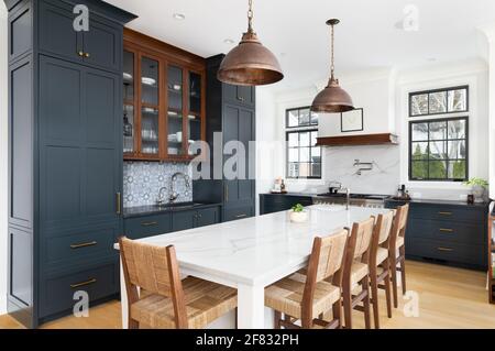 Une cuisine luxueuse avec des armoires bleues, des plafonniers en bronze suspendus au-dessus de la grande île blanche, des appareils de luxe, et un fond de carrelage. Banque D'Images