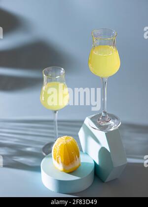 Limoncello, liqueur italienne traditionnelle sur fond de béton léger aux rayons du soleil. À côté, il y a un citron jaune, des agrumes frais. Compo Banque D'Images