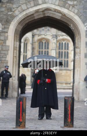 Un gardien du château abrite sous un parapluie à la porte Henry VIII du château de Windsor, dans le Berkshire, à la suite de l'annonce, le vendredi 9 avril, de la mort du duc d'Édimbourg à l'âge de 99 ans. Date de la photo: Dimanche 11 avril 2021. Banque D'Images