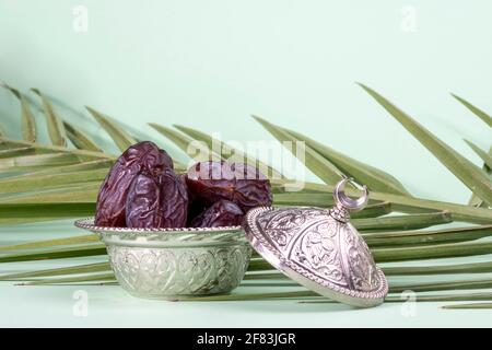 Festival islamique religieux et mois Saint du Ramadan, EID KAREEM, concept: Un bol d'argent avec des fruits secs. Le palmier laisse sur fond vert Banque D'Images