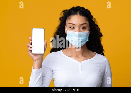 Carte du coronavirus. Femme noire portant un masque médical montrant un smartphone avec écran blanc Banque D'Images