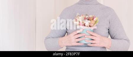 Une femme blanche sans visage en col de cygne gris tenant dans ses mains un beau bouquet de fleurs séchées. Bannière Banque D'Images